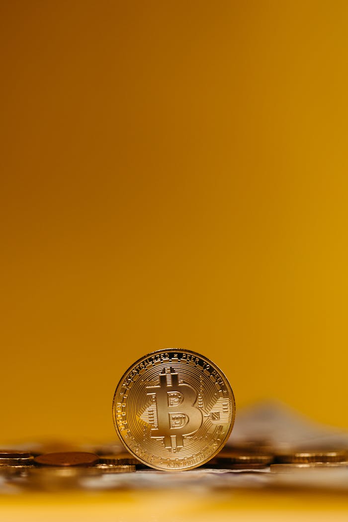 Close-up of a Bitcoin coin standing upright on a blurred yellow background, symbolizing digital finance.